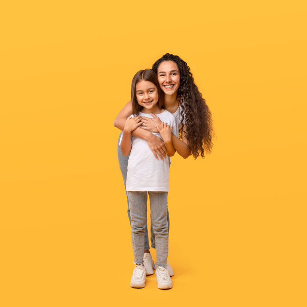 Happy Arabic Mother Hugging Little Daughter Standing Over Yellow Background - Foto, Imagem