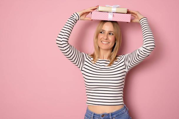 Portrait of a smiling pretty young woman holding gift boxes isolated over pink background - Foto, Imagem
