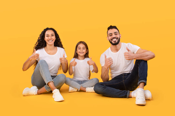 Família árabe alegre Gesturing Polegares para cima aprovando algo, fundo amarelo - Foto, Imagem