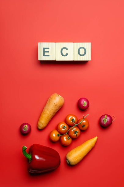Κάτοψη των οικολογικών γραμμάτων σε ξύλινους κύβους κοντά σε φρέσκα λαχανικά σε κόκκινο φόντο  - Φωτογραφία, εικόνα