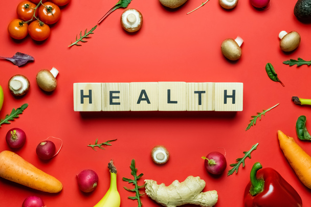 Flat lay with health lettering on wooden cubes near organic vegetables and fruits on red background  - Foto, Imagem
