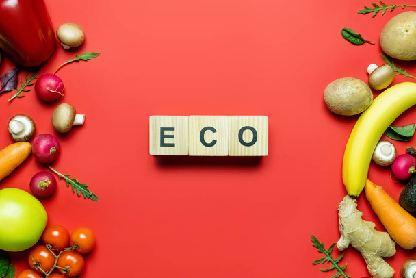 Vista superior de cubos con letras ecológicas cerca de frutas y verduras maduras sobre fondo rojo  - Foto, imagen
