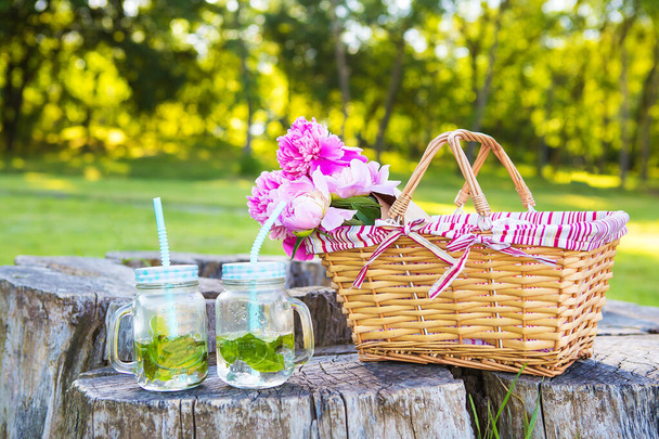 Красива кошик стоїть на дерев'яному пні з квітами і напоями
 - Фото, зображення