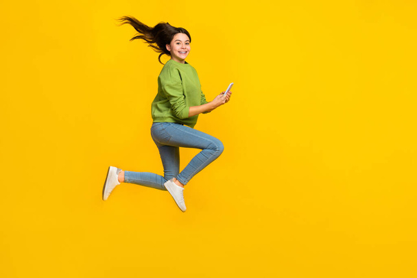 Full body profile side photo of young girl jump energetic use mobile share app isolated over yellow color background - Fotografie, Obrázek