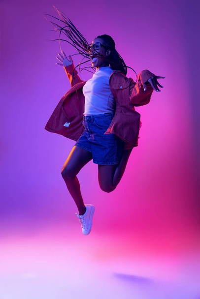 Studio shot of young excited woman in casual style outfit jumping isolated on purple background. Concept of beauty, art, fashion, youth, style - Photo, image