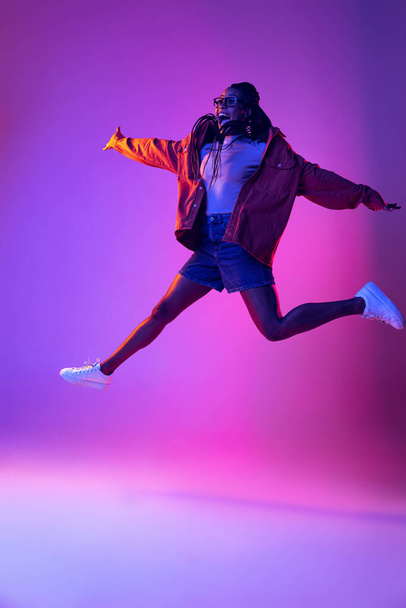 Studio shot of young excited woman in casual style outfit jumping isolated on purple background. Concept of beauty, art, fashion, youth, style - 写真・画像