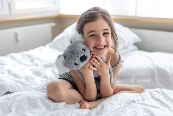 Happy little girl with soft toy koala in bed. - Fotó, kép