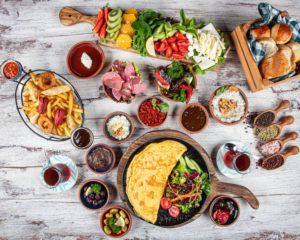 Turkish breakfast table. Pastries, vegetables, greens, olives, cheeses, omelette, spices, jams, honey, tea in a thermos, large composition. Breakfast concept in restaurant and cafe. - Photo, Image