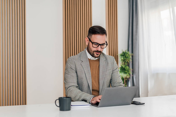 Magabiztos üzletember, aki laptopon dolgozik. Koncentrált férfi vállalkozó visel formális. Az irodájában ül az asztalnál.. - Fotó, kép