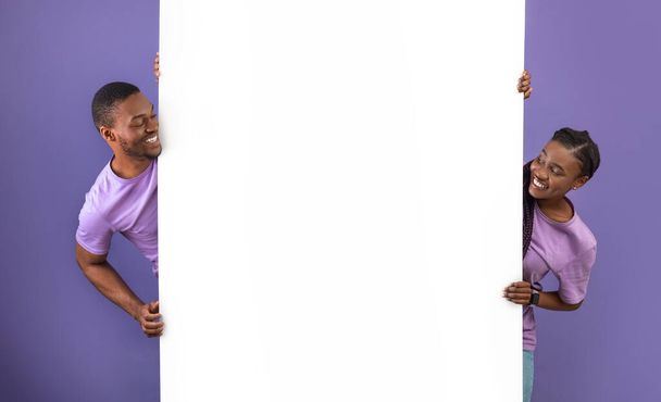 Черная пара держит и смотрит на пустой белый рекламный плакат - Фото, изображение