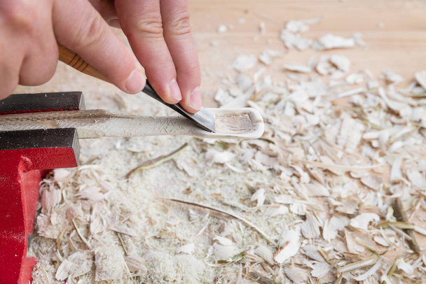 Samořezaná dřevěná lžíce upnutá ve svěráku opracovaná nožovým nástrojem na pracovním stole s dřevěnými štěpkami, Německo - Fotografie, Obrázek