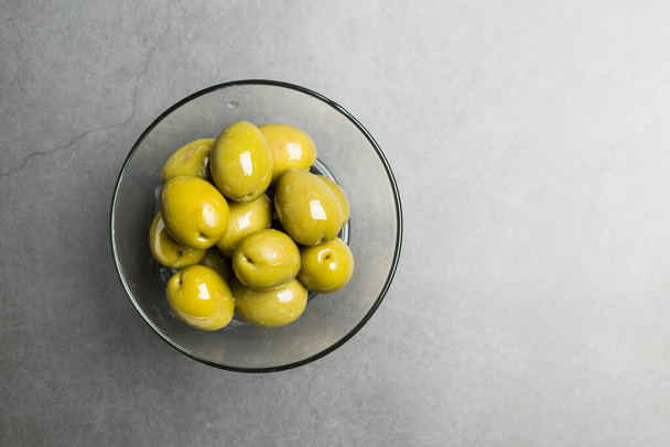 Big green olives in glass bowl on stone table, top view. - Fotó, kép
