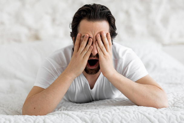 Крупный план бородатого человека, лежащего в постели, зевающего - Фото, изображение