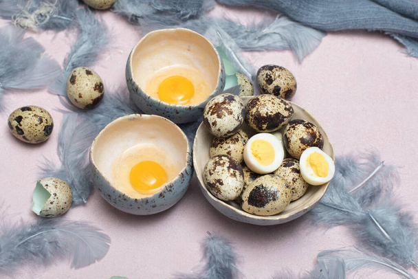 křepelčí vejce v keramických vázách, šedé peří na stole, velikonoční zátiší, - Fotografie, Obrázek