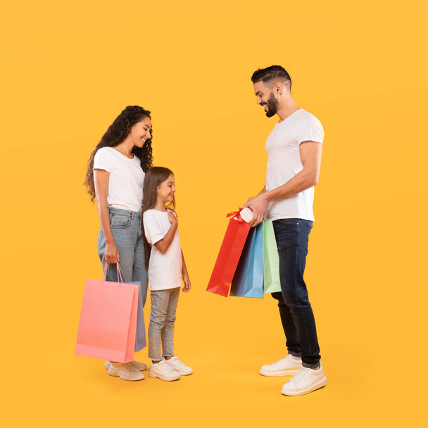 Padres dando regalos y bolsas de compras a la hija, fondo amarillo - Foto, Imagen