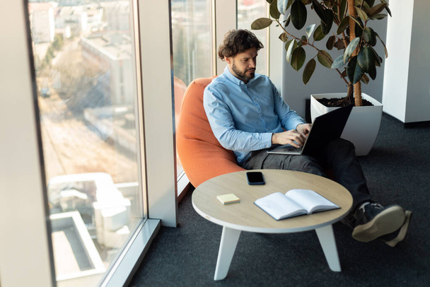 Empresário usando laptop sentado em saco de feijão no escritório - Foto, Imagem