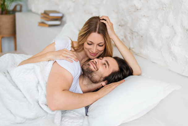 Прихильна молода жінка обіймає свого хлопця після пробудження вранці, лежачи на ліжку вдома
 - Фото, зображення