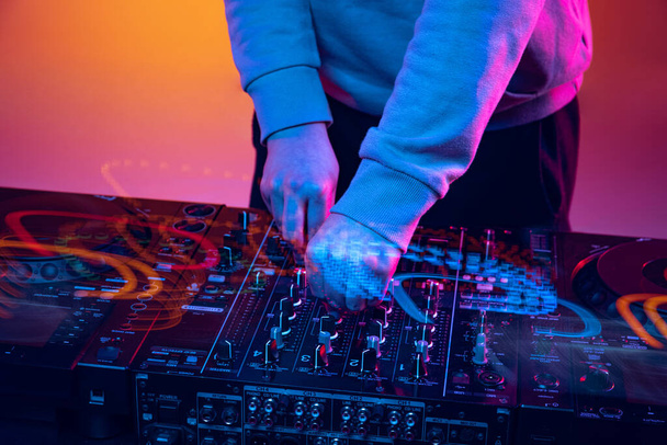 Close-up image in neon lights. Male hands turning sounds on professional dj mixer. Mixed lights effect - Photo, Image