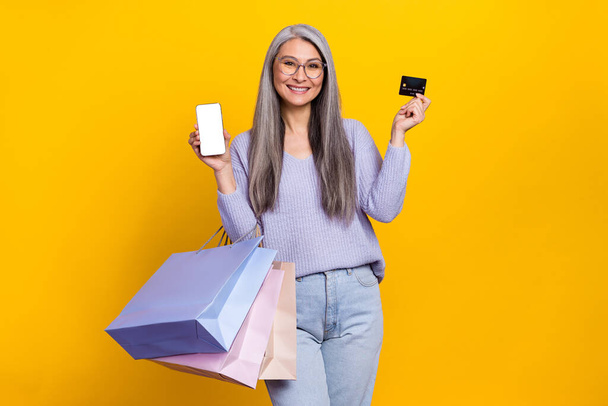 Photo of charming grey haired casual style grandma recommend you eshop online payment isolated on yellow color background - 写真・画像