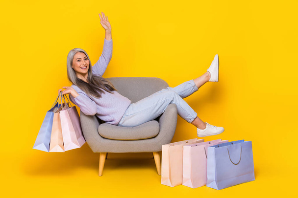Photo of funny shiny lady pensioner dressed pullover sitting cozy chair rising bargains isolated yellow color background - Valokuva, kuva