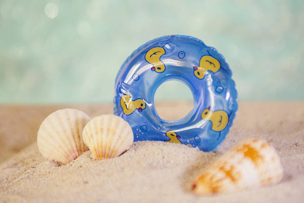 Decorative swimming circle and sea shells staying in sand.Good as background for text overlay. - Photo, image