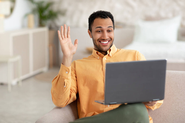 Smiling man working on laptop waving hand - Foto, afbeelding