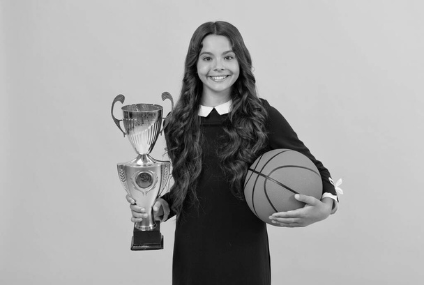 陽気な子供は黄色の背景にバスケットボールボールとチャンピオンカップを保持し、スポーツの成功 - 写真・画像