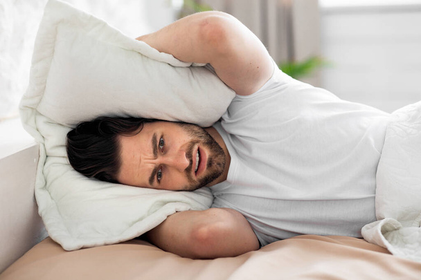 Young man in bed covering head with pillow - Foto, afbeelding