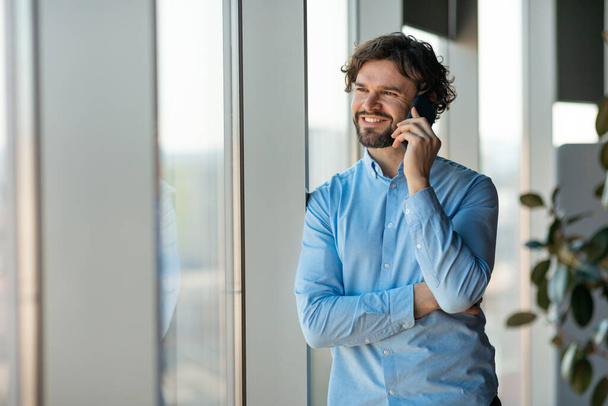 Χαμογελώντας επιχειρηματίας που εργάζεται και μιλάει στο τηλέφωνο στο γραφείο - Φωτογραφία, εικόνα