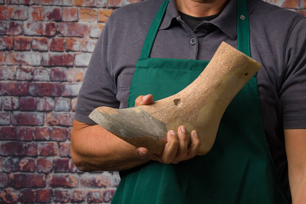 крупним планом руки ортопедичного взуття, що представляє індивідуальне дерев'яне останнє в стіні своєї майстерні
 - Фото, зображення