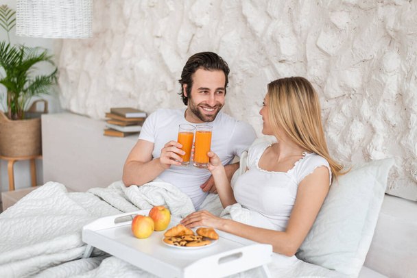 Happy millennial couple having breakfast in bed together, spending honeymoon at hotel, copy space - Foto, imagen