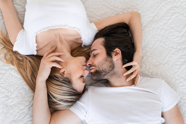 Draufsicht auf das liebende Millennial-Paar, das auf dem Bett schläft, Lippen berührt und kuschelt. Konzept Liebe und Beziehungen - Foto, Bild