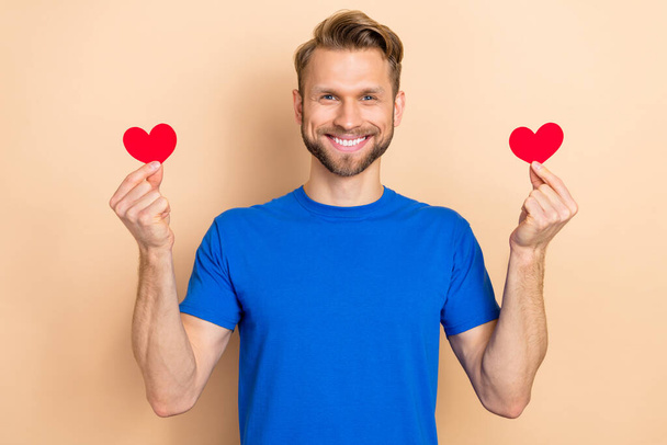 Photo of young cheerful guy hold little paper heart shape romantic cardiac isolated over beige color background - Фото, зображення