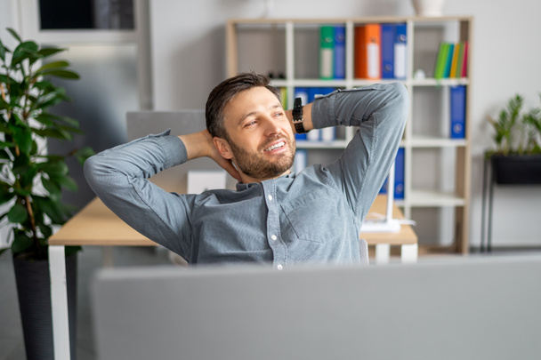 Successful businessman. Relaxed mature man holding hands behind head, sitting at desk in modern office - Φωτογραφία, εικόνα