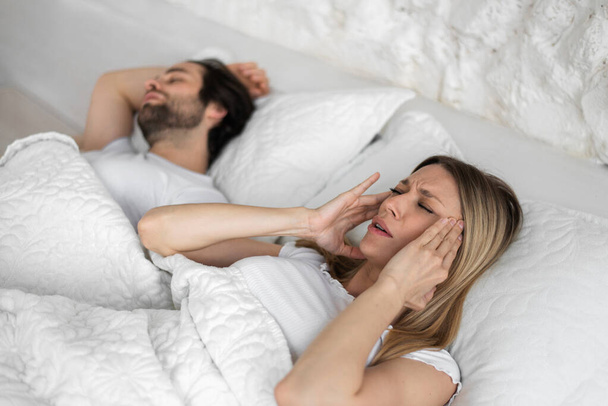 Mujer joven irritado molesto por sus maridos roncando, cubriendo las orejas en la cama en casa, espacio de copia - Foto, imagen