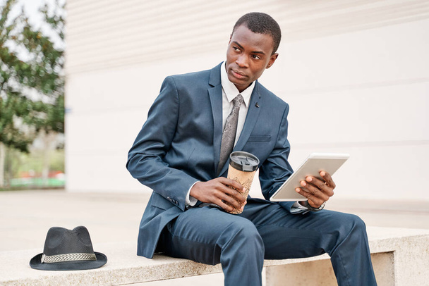 Young smart businessman using a digital tablet and analyse information on a bench in the city. Working outside and Mobile office business concept. - Photo, Image
