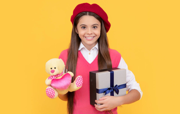 happy teen girl in french beret hold toy present and gift box on yellow background, black friday - Foto, Imagem