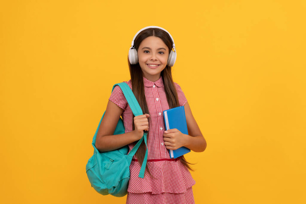 boldog iskola tini lány fejhallgató hordozza hátizsák és munkafüzet, elearning - Fotó, kép