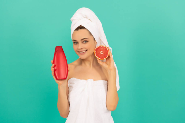 щаслива жінка в рушнику з пляшкою шампуню з грейпфрутом на синьому фоні
 - Фото, зображення