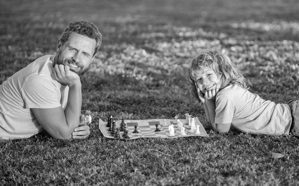 ευτυχισμένη οικογένεια του πατέρα και του γιου αγόρι παίζουν σκάκι στο πράσινο γρασίδι στο πάρκο εξωτερική, χαλαρώστε - Φωτογραφία, εικόνα