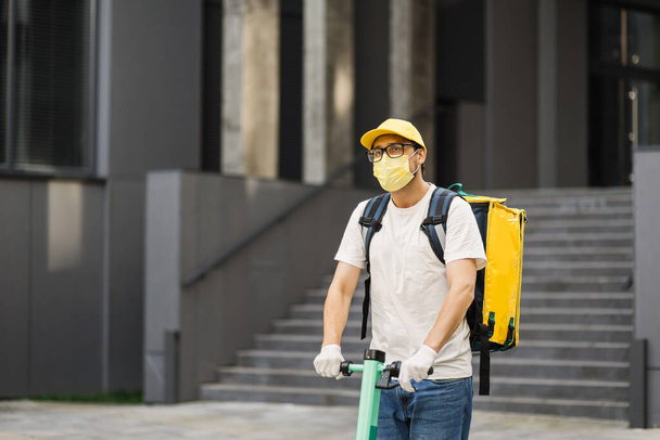 Courier deliver food on electric scooter wearing yellow facial protective mask. - 写真・画像