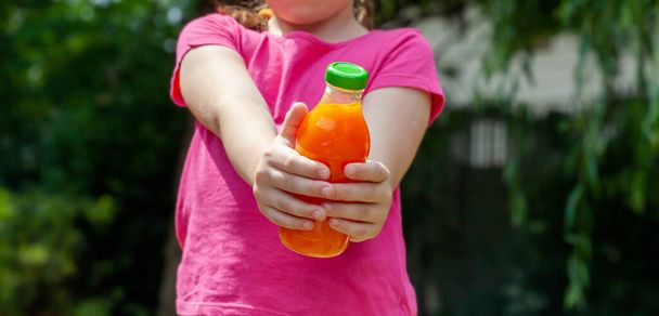 Anonymes junges, nicht wiedererkennbares Schulkind, Mädchen mit einer Glasflasche voll orangefarbenem Gemüsesaft in der Hand, Weitschuss, Objektnahaufnahme. Schenken, ein Getränk reichen, Vitamine, gesunde Getränke - Foto, Bild