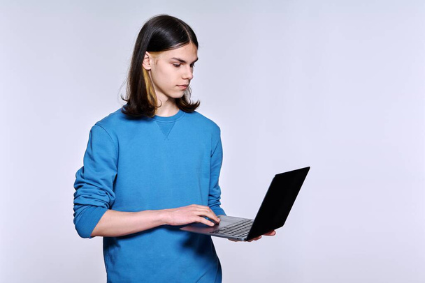 Teenage male student using laptop, light studio background - Photo, image