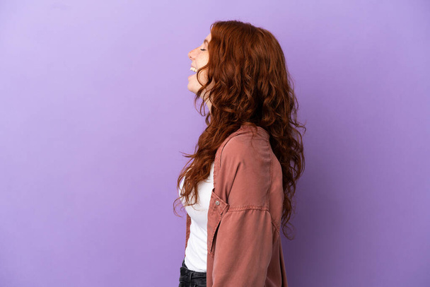 Teenager redhead girl over isolated purple background laughing in lateral position - Фото, изображение