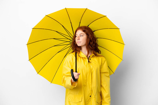 Teenager zrzka dívka nepromokavý kabát a deštník izolované na bílém pozadí při pohledu na stranu - Fotografie, Obrázek