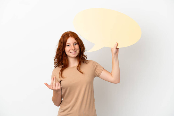 Teenager redhead girl isolated on white background holding an empty speech bubble and doing coming gesture - Zdjęcie, obraz
