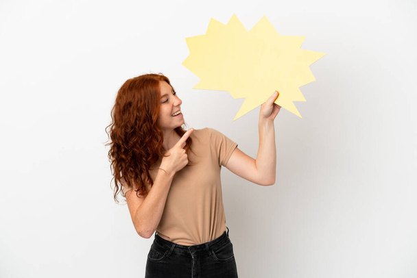 Teenager redhead girl isolated on white background holding an empty speech bubble and pointing it - Photo, Image