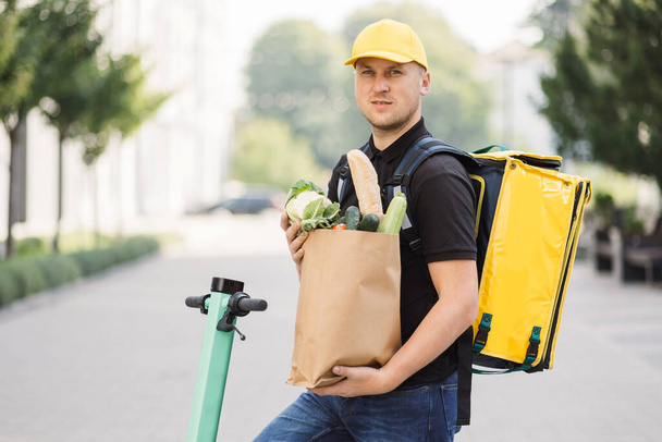 Food delivery electric scooter driver holding paper bag with organic fresh vegetables - Фото, изображение