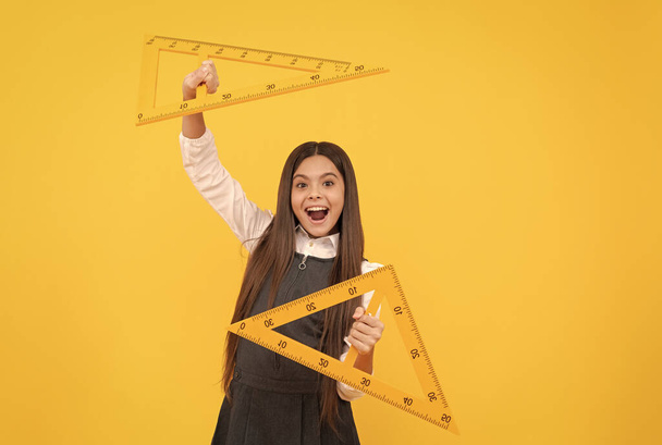 幸せな子供は黄色の背景に学校で数学三角形の支配者を保持します - 写真・画像