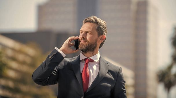 successful businessman in suit speaking on phone standing outdoor, communication - Fotografie, Obrázek